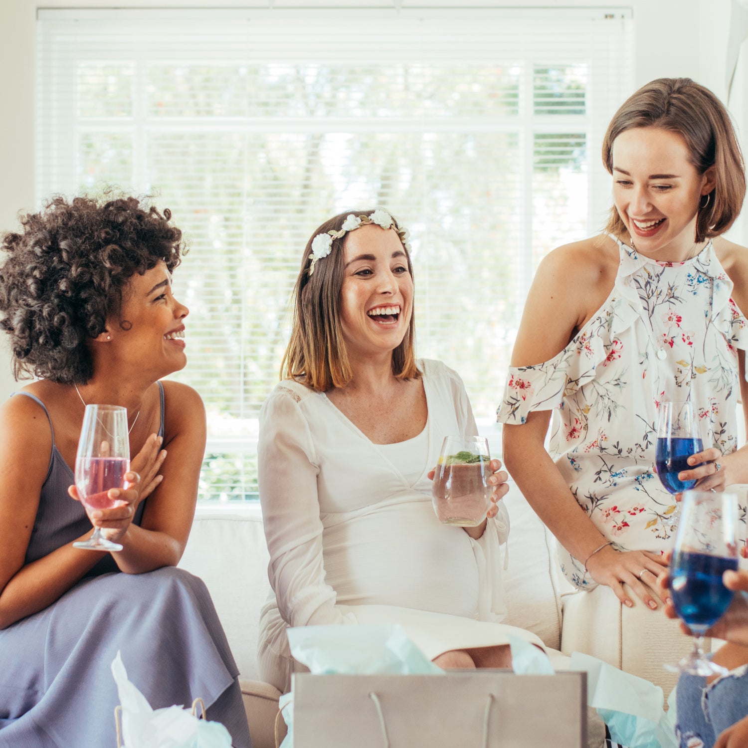 three friends with drinks in hands celebrating the pregnancy of the lady in the middle.