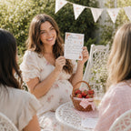 Pregnant mum holding Berry Sweet Baby strawberry prediction card during a baby girl garden baby shower with guests.
