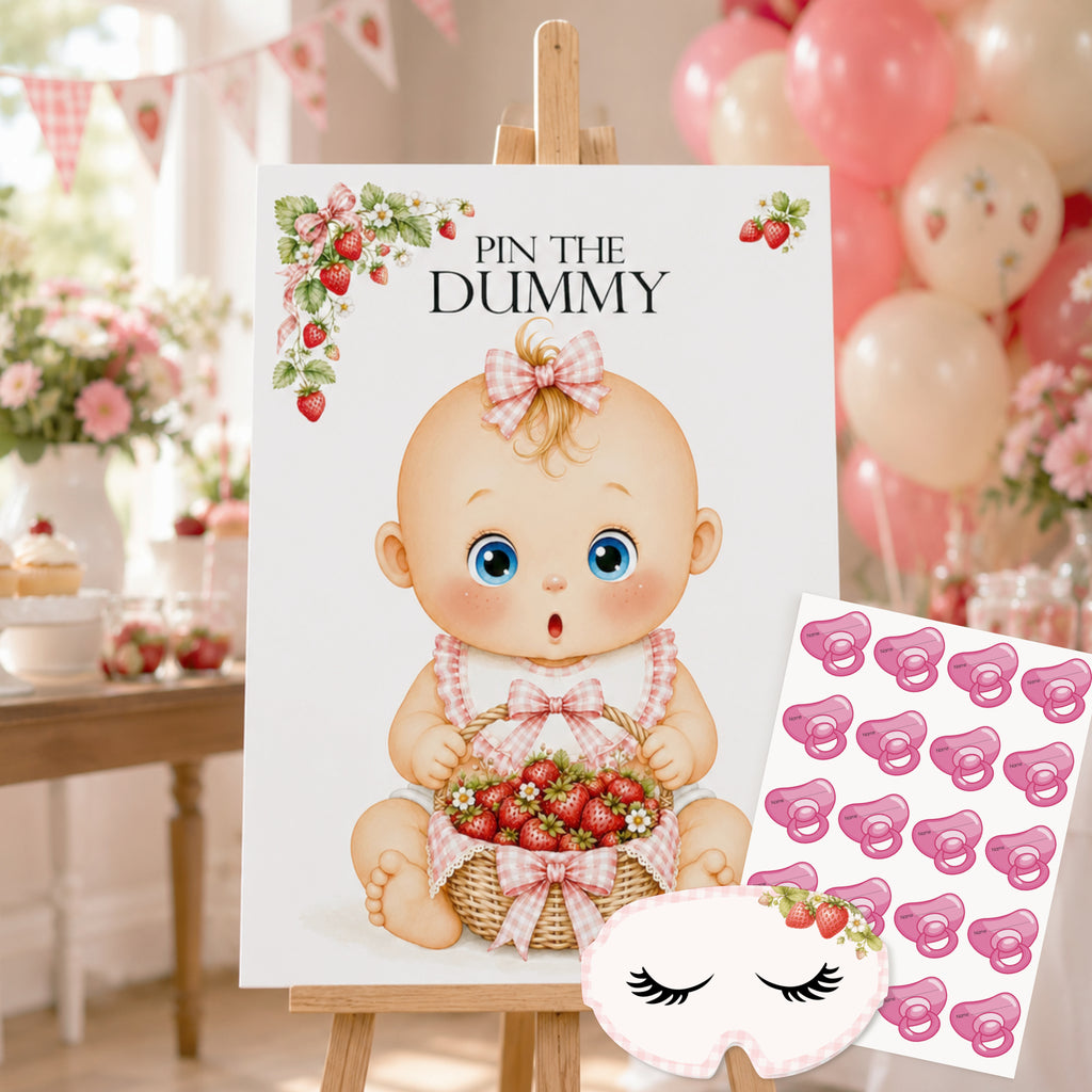 A baby shower game board or sign on an easel that reads 'PIN THE DUMMY,' featuring a cartoon baby holding strawberries. A sheet of pink pacifier stickers and a matching sleep mask are placed beside it, with a softly blurred party background of balloons, flowers, and bunting.
