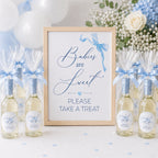 Mini bottles of alcohol with blue ribbons and a sign reading 'Babies are Sweet, Please Take a Treat' at a baby shower. 