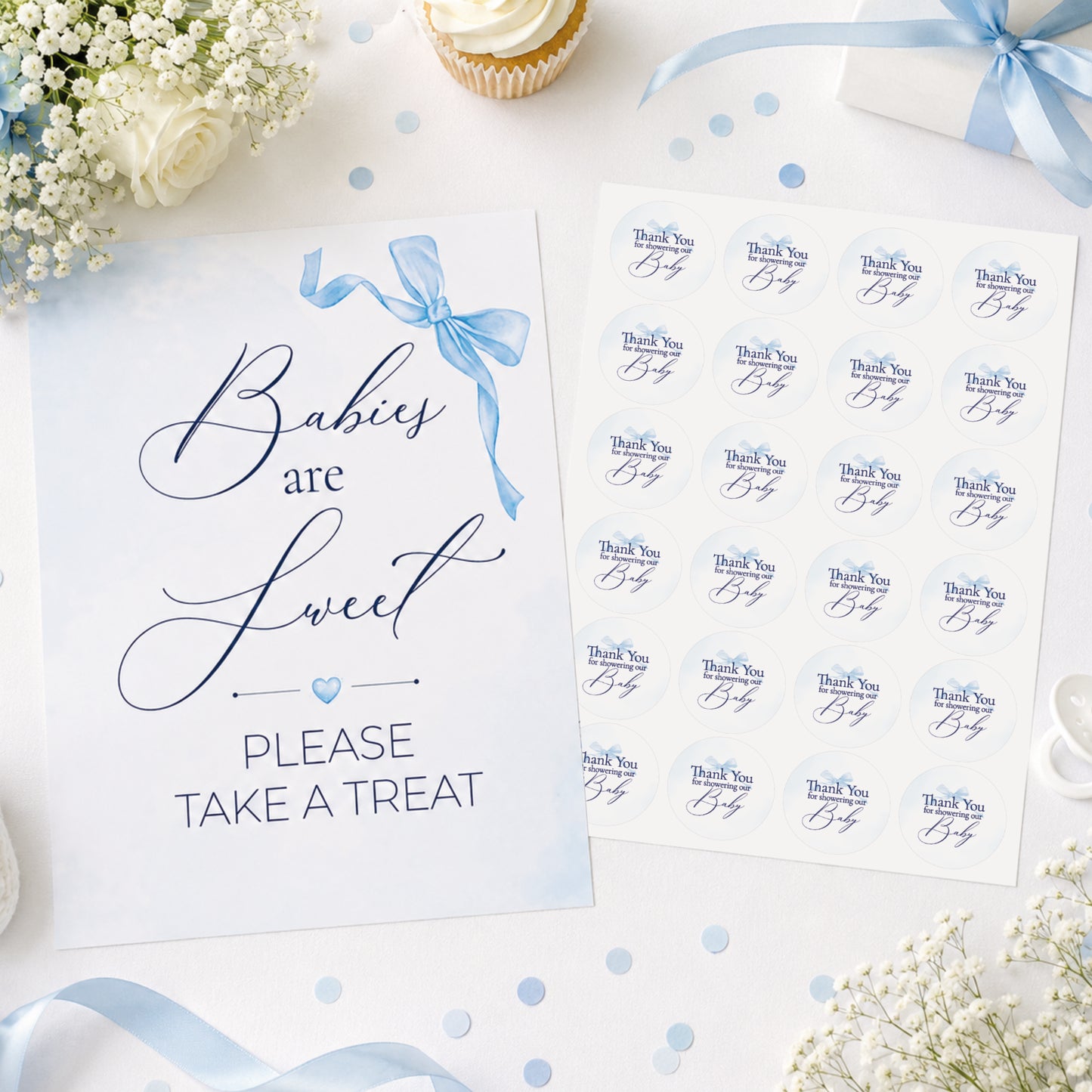 Blue bow baby shower sign and matching 37mm favour stickers styled on a baby shower table with flowers, ribbons and party treats