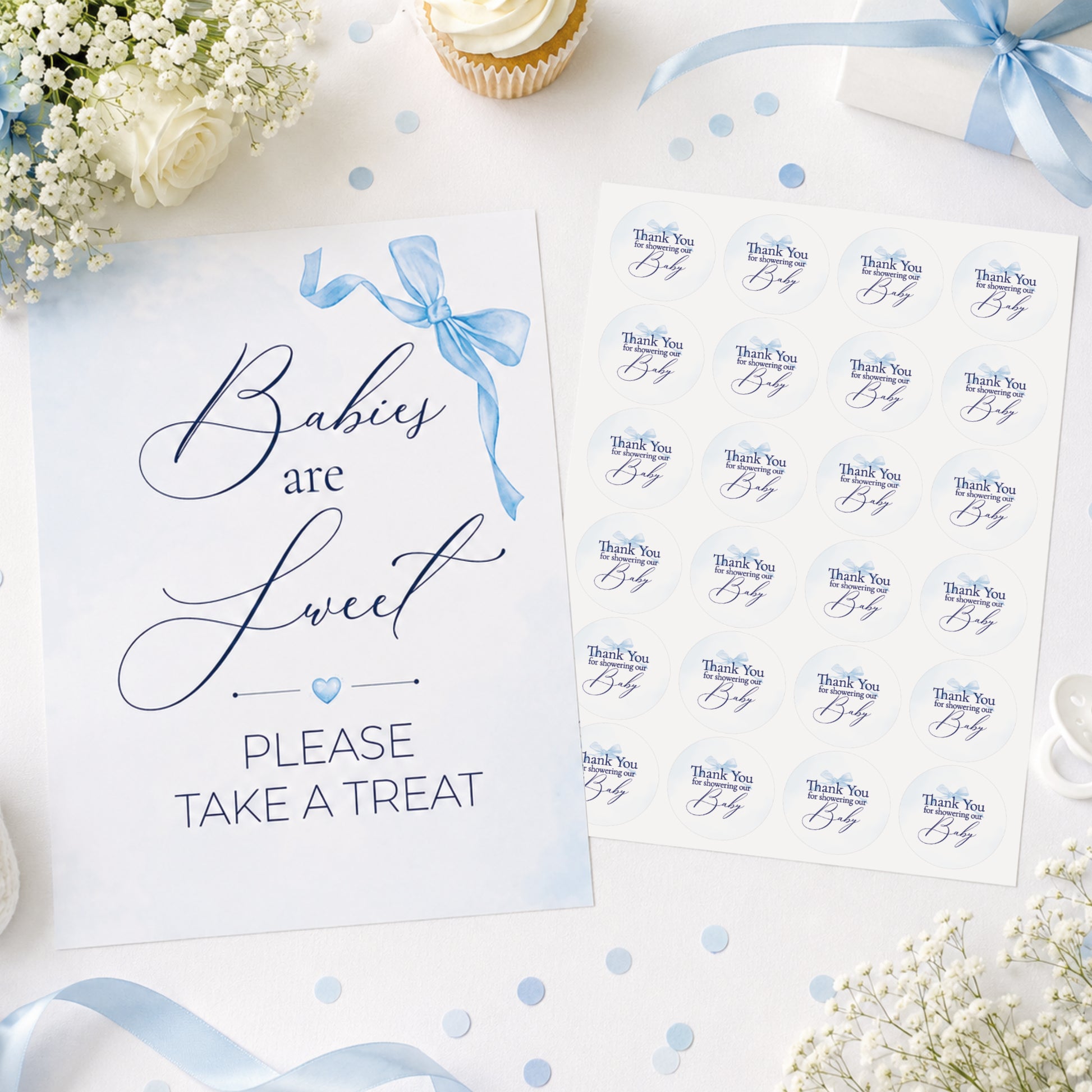 Blue bow baby shower sign and matching 37mm favour stickers styled on a baby shower table with flowers, ribbons and party treats