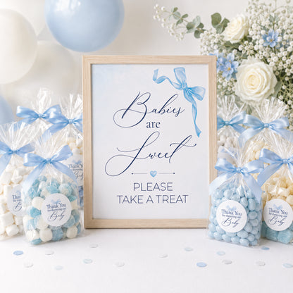 Blue bow baby shower treat table sign with matching favour stickers displayed alongside sweet bags and baby shower party favours