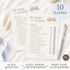 Two printed 'Mummy or Daddy' game cards laid on a white fabric surface with a blue ribbon, a gold pen, and a round badge reading '10 PLAYERS'. The cards show playful prompts, score lines, and small teddy bear illustrations.