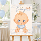 A baby shower sign featuring an illustration of a cute baby sitting on clouds with the text 'Pin the Dummy', displayed on a wooden easel in a decorated party setting.