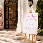 A custom baby shower welcome sign on a wooden easel, set outdoors in front of a white building entrance with balloon decorations and a garden.