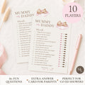 A set of 'Mummy or Daddy' baby shower game cards displayed on a light wood surface next to a pink ribbon and pen. The image includes promotional text overlays indicating '10 PLAYERS' and '16+ FUN QUESTIONS'.