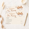 A baby advice card for 'Mummy' styled in a flat-lay arrangement with a gold pen, a lit candle, dried grass, and a beige ribbon on a white marble surface. The card features watercolor illustrations of a teddy bear sleeping on a cloud with a crescent moon, with text fields for writing personal messages.