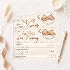A baby advice card for 'Mummy' styled in a flat-lay arrangement with a gold pen, a lit candle, dried grass, and a beige ribbon on a white marble surface. The card features watercolor illustrations of a teddy bear sleeping on a cloud with a crescent moon, with text fields for writing personal messages.