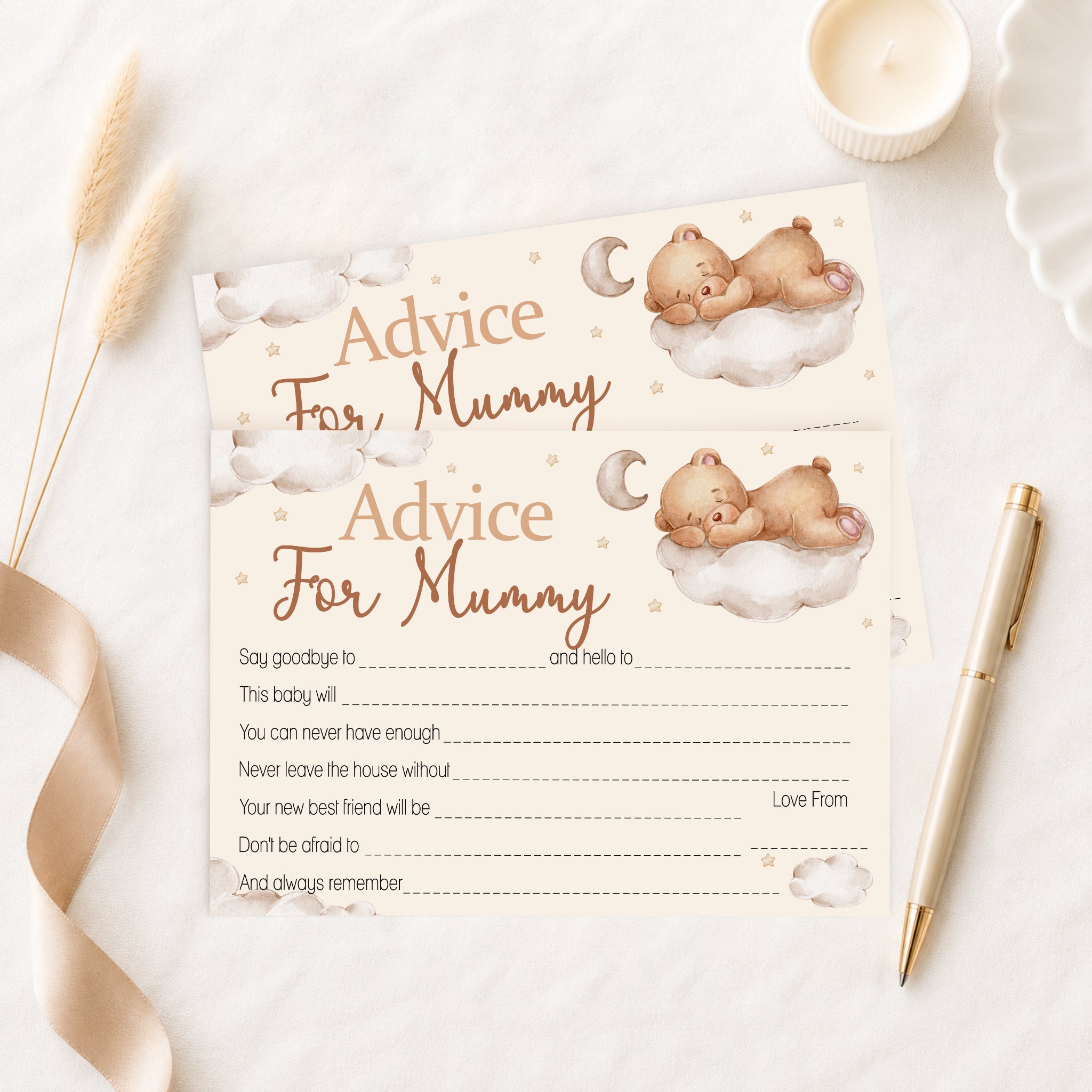 A baby advice card for 'Mummy' styled in a flat-lay arrangement with a gold pen, a lit candle, dried grass, and a beige ribbon on a white marble surface. The card features watercolor illustrations of a teddy bear sleeping on a cloud with a crescent moon, with text fields for writing personal messages.