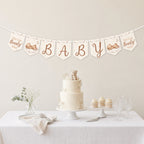 Teddy bear baby shower banner bunting displayed above a neutral baby shower dessert table with teddy bear cake.