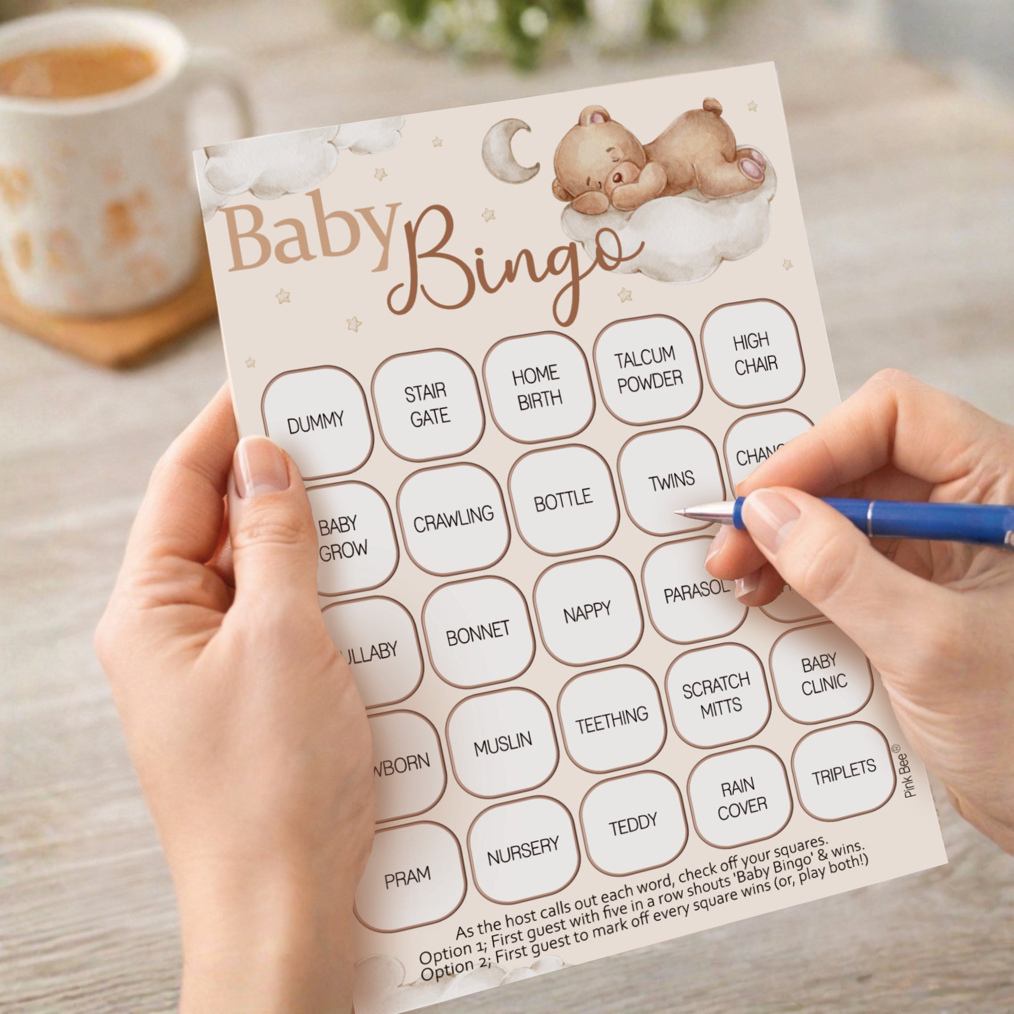 Hand holding Teddy Bear Baby Shower Bingo card at elegant neutral teddy bear themed baby shower venue with luxury party décor.