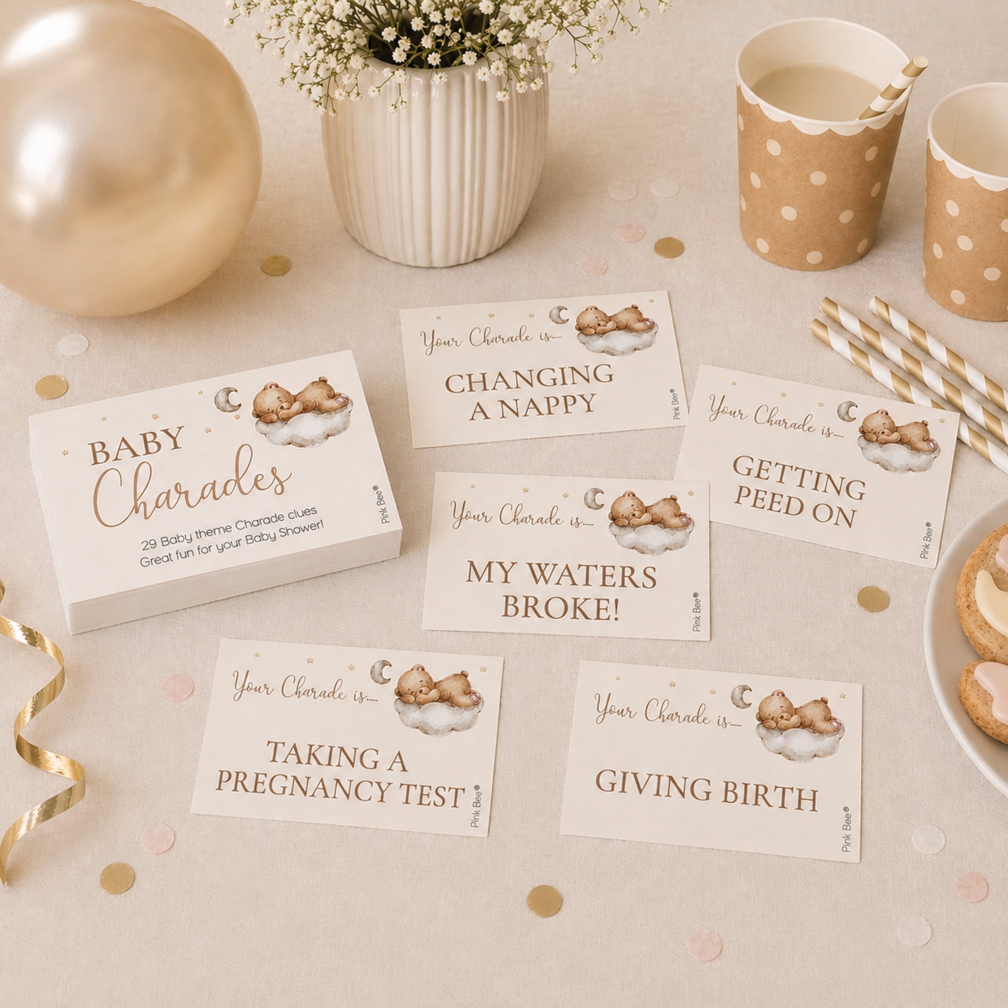 Teddy bear baby shower charades game cards displayed on a neutral party table with balloons, cups and baby shower decorations.