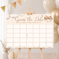 Teddy Bear Guess the Date baby shower poster displayed on a wooden easel with neutral cream and gold baby shower decorations.
