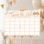 Teddy Bear Guess the Date baby shower poster displayed on a wooden easel with neutral cream and gold baby shower decorations.