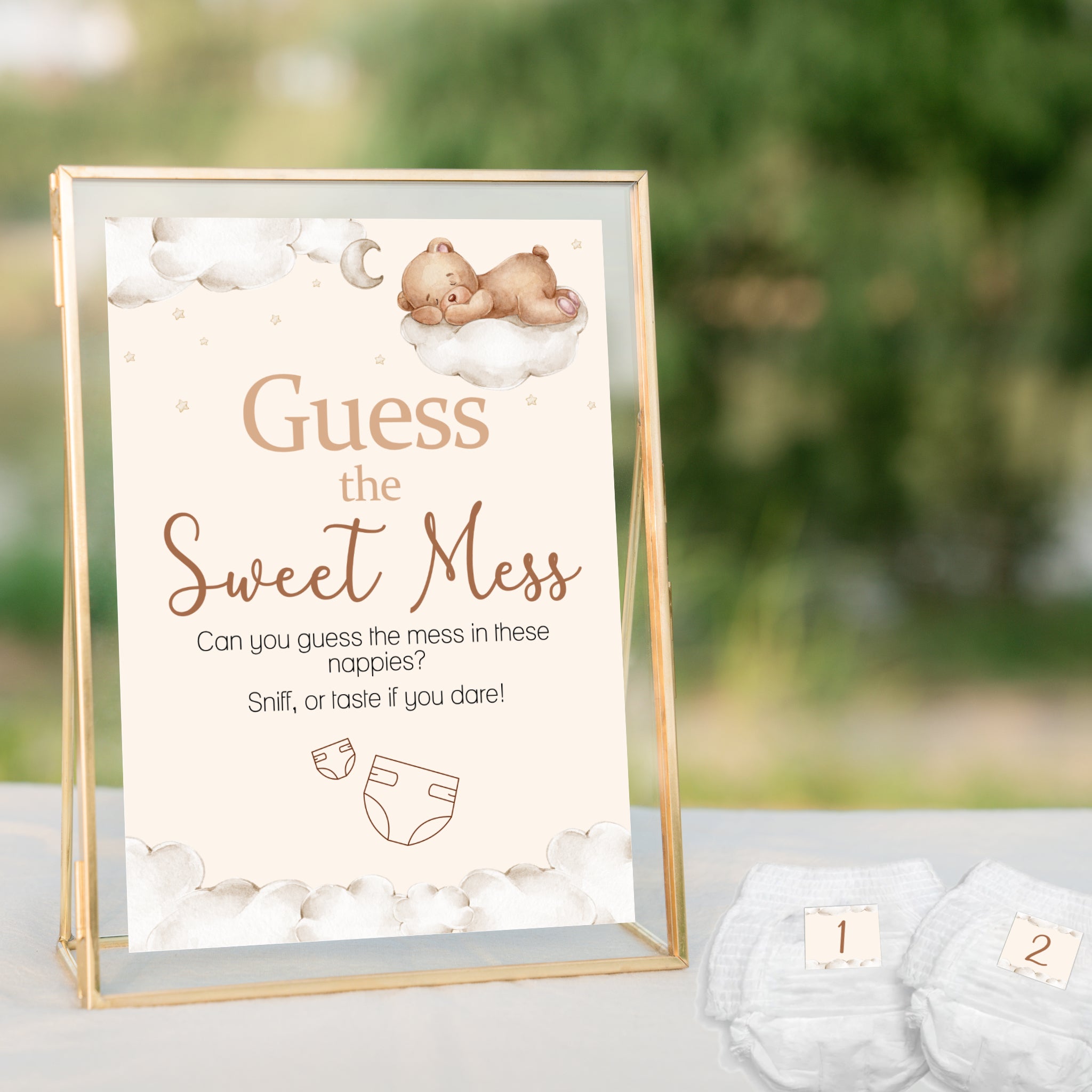 Teddy Bear Guess the Sweet Mess baby shower sign displayed in a gold frame beside numbered nappies for a neutral teddy themed baby shower.